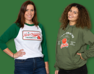 Two women smiling against a green background. One wears a white and green baseball tee, the other a green hoodie. Both shirts feature "A New Orleans Favorite" text with a flower graphic.