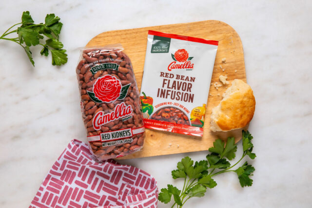 Bag of Camellia red kidney beans and a packet of Red Bean Flavor Infusion on a wooden board, with fresh parsley and a biscuit nearby, creating a homey feel.