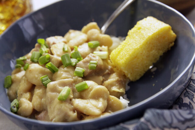 Creamy butter beans topped with chopped green onions in a deep blue bowl, served with a slice of yellow cornbread, conveying a cozy, home-cooked meal.