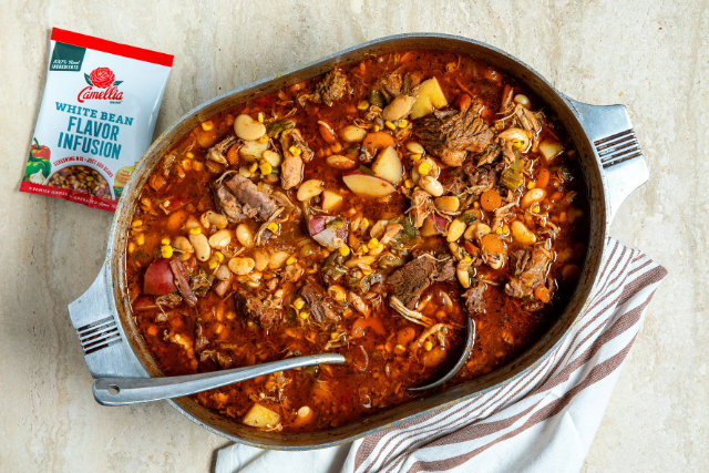 Hearty beef and bean stew with vegetables in a rustic pot beside a seasoning packet. The meal looks warm and inviting, perfect for comfort food.