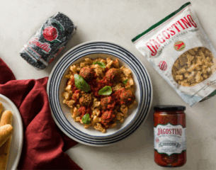 Plate of pasta with meatballs topped with sauce and basil is centered. Surrounding are packages of pasta, black beans, red cloth, and a jar of sauce.