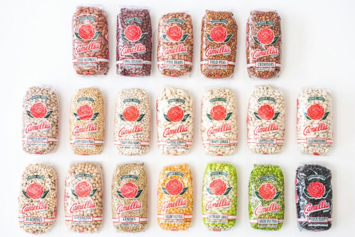 Sixteen bags of Camellia beans, peas, and lentils are arranged in rows on a white background. Each bag displays a red rose logo.