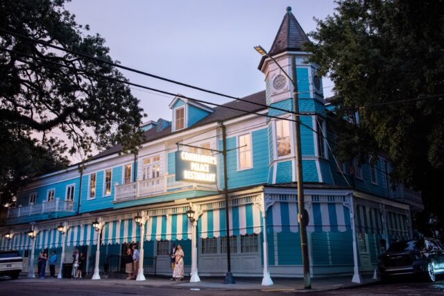 A vibrant turquoise Victorian-style building with white trim and striped awnings, surrounded by trees.