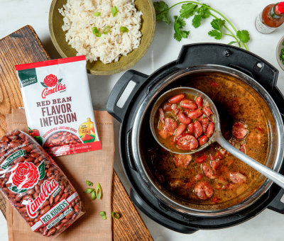 A pot of cooked red beans and sausage stew on a wooden board. Beside it, Camellia red kidney beans and flavor infusion packets are displayed.