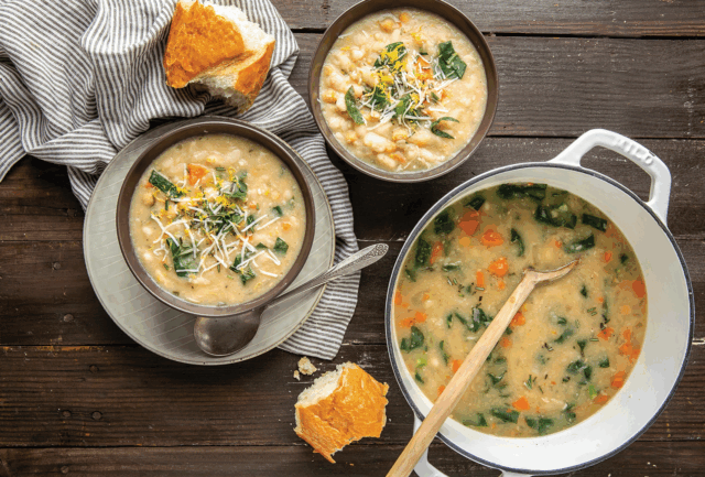 Big pot of soup with two small bowls of soup next to it with broken bread 