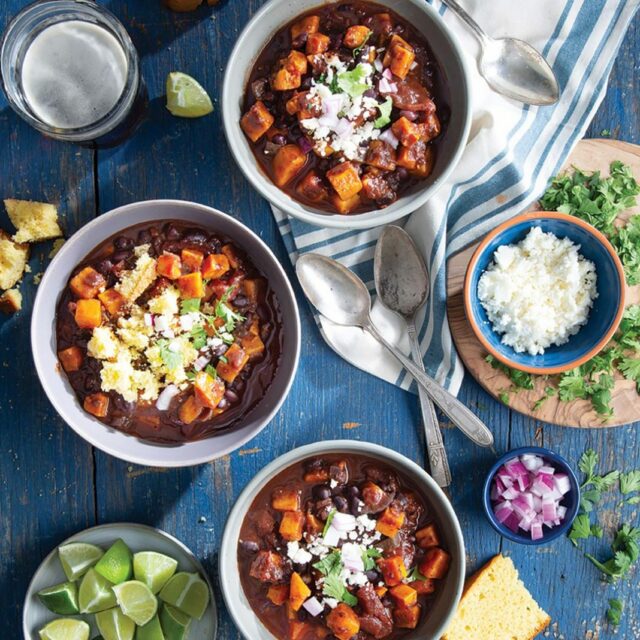 Three bowls of chili surrounded by spoons and ingredients