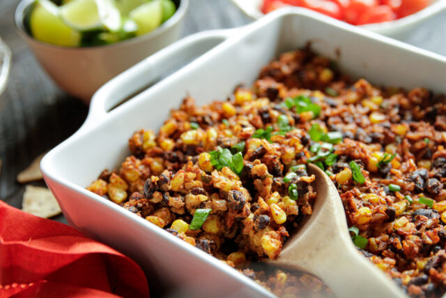 Casserole in a dish with a wooden spoon next to a bowl of limes
