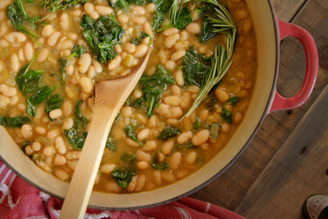 Close-up of a pot of white beans with spinach with a wooden spoon inside