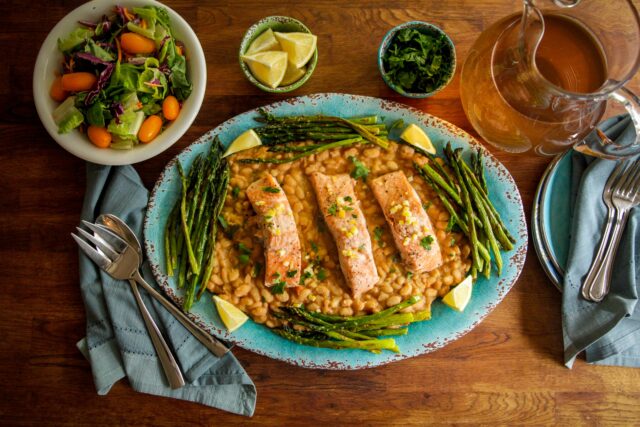 Salmon and beans on a blue plate next to a small plate of vegetables