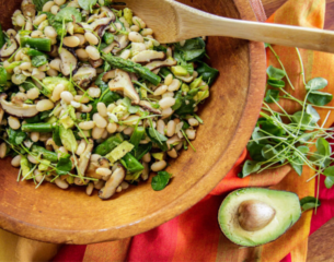 A bowl filled with beans, mushrooms, and greens, accompanied by a wooden spoon resting on the side.