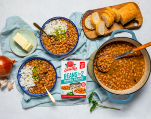 Three bowls of assorted beans alongside slices of bread and butter on a wooden table.
