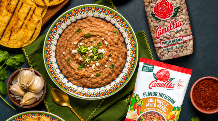 Camellia Pinto Beans and Southwest Pinto Beans Flavor Infusion on a wooden board with garlic, onion, and herbs, alongside refried pinto beans and tortillas.