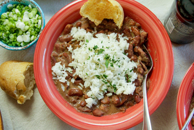 Red beans and rice topped with white rice and served with cornbread and chopped green onions in a red bowl.