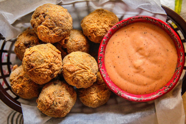 Basket of fried boudin balls served with creamy remoulade dipping sauce in a red bowl.
