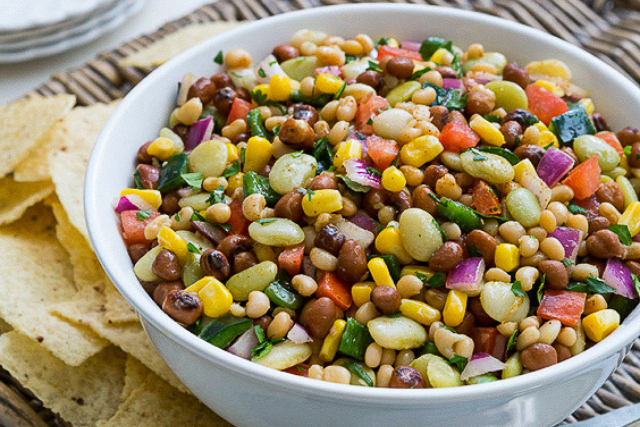 Colorful bean salad with lima beans, corn, bell peppers, and red onions in a white bowl, served with tortilla chips.