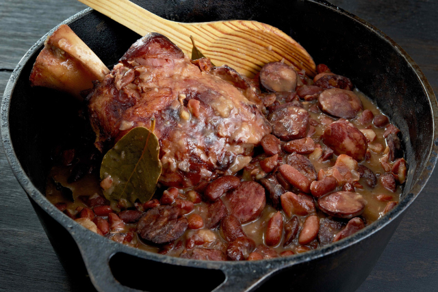 Red beans and sausage simmering in a cast iron Dutch oven with ham hock, sliced andouille sausage, and bay leaves.