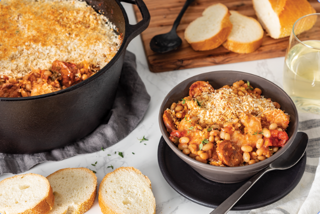 White bean cassoulet with breadcrumb topping in cast iron pot and bowl, served with sliced French bread and white wine.
