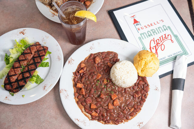 Red Beans on w white plate next to a plate of meat and a menu and drink