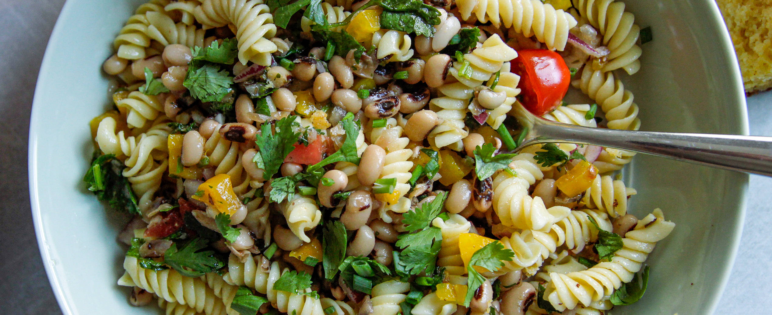 close up of A bowl of vibrant and fresh pasta, black eyes, cilantro, corn and cornbread