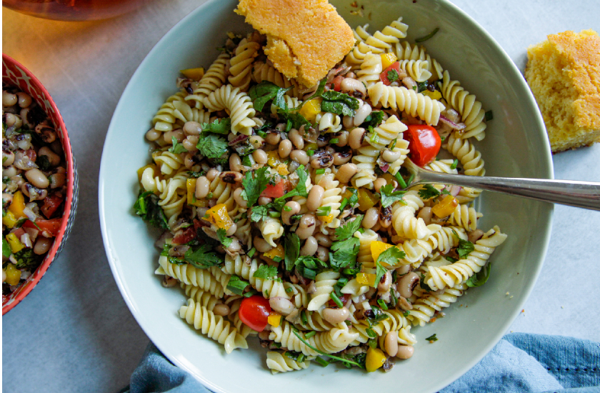A bowl of vibrant and fresh pasta, black eyes, cilantro, corn and cornbread